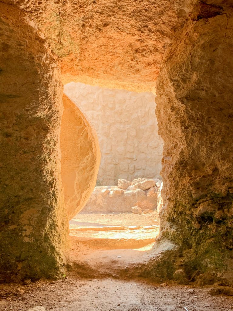 Doorway hewn into rock, with a circular stone partially rolled away and light shining through